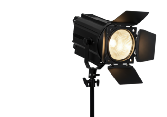 A black metallic studio Fresnel spotlight with open barn doors emitting bright warm white light on a black stand, isolated against a clean transparent studio background with copy space,