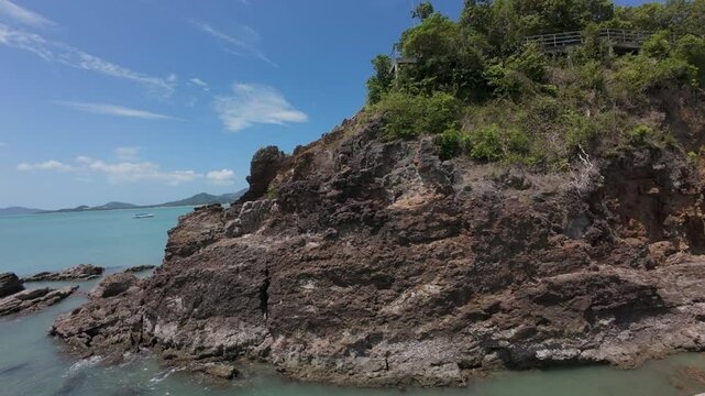Aerial View of Tropical Road Winding Along Rocky Shoreline with Dense Green Foliage and Clear Turquoise Sea for Scenic Eco Travel Concept