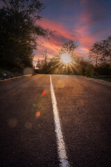 Empty road leading into the sunset with sun flares and dramatic sky, symbolizing journey, hope, and...