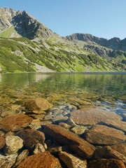Crystal Clear Mountain Lake with Rocky Shore and Green Hills