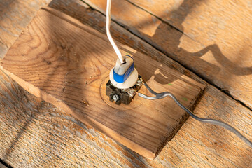 Old, potentially hazardous electrical outlet is attached to a weathered wooden surface,...
