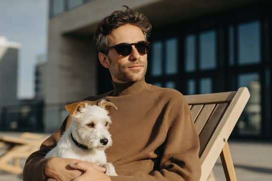 Young caucasian male with sunglasses relaxing outdoors holding small white dog
