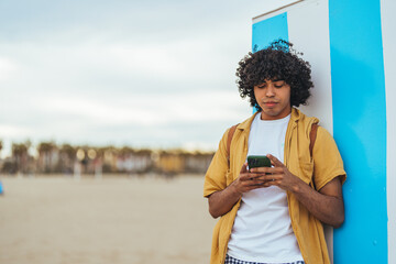 Young Man Using Smartphone Outdoors on a Sunny Beach Day