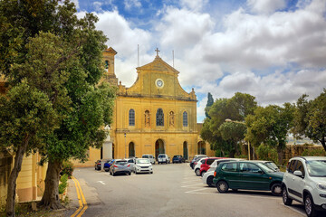 Facade of a historic church in baroque style with bell tower and clock , surrounded by trees and...