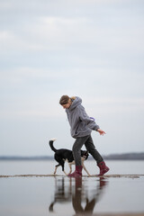 A woman in a hoodie and boots walks with her border collie along a pier. The water is calm and...