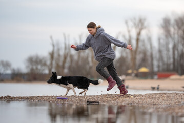 A young woman in casual clothes sprints along a beach near the water with her energetic black and...