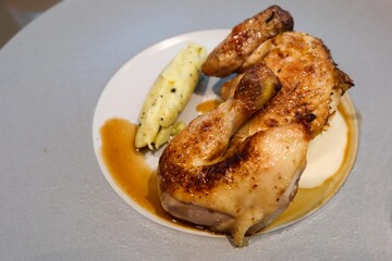 a portion of roasted chicken, golden and crispy on the outside, accompanied by a smooth, creamy serving of mashed potatoes with a drizzle of savory sauce  on a white and grey plate
