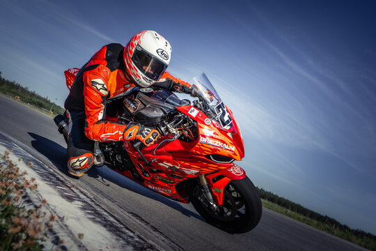 A Motorcyclist in Orange and White Leans into a Turn on an Open Road