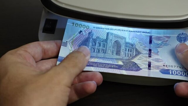 Examination of Uzbekistan Sum (UZS) cash money with UV counterfeit detector. Concept of authenticity check, fight against counterfeiting of banknotes, anti fraud measures in Uzbekistan. Close up view.