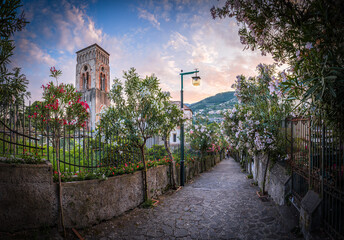 A cobblestone path in Ravello, Amalfi Coast, Italy, at sunset, framed by oleanders and a medieval...