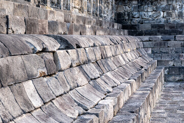 Stone seating structure at Borobudur Temple with worn, curved blocks and ancient carvings above.