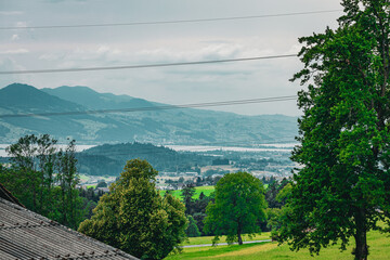 Scenic panoramic view of the Swiss countryside featuring green hills, trees, rooftops, and a...