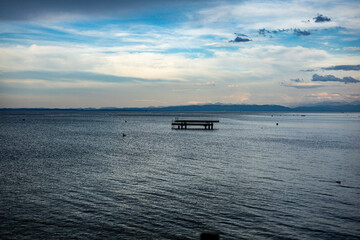 Tranquil lake landscape with a wooden dock floating on still water under a dramatic evening sky....