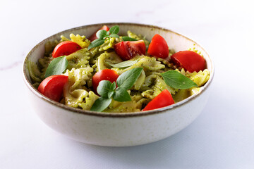 Aromatic homemade vegan farfalle with green pesto sauce, cherry tomatoes, basil leaves and homemade spcy olive oil close up Healthy vegan food concept.