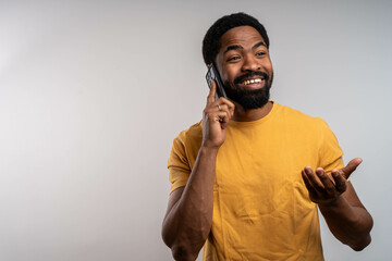 Smiling handsome black man having pleasant phone conversation on smartphone, casual and positive communication, isolated studio background