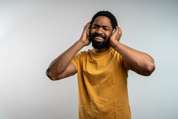 Smiling young black man enjoying music with wireless headphones, cheerful expression, isolated...