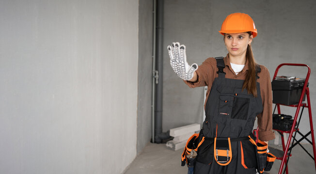 Female builder or repairman wears helmet and overalls showing stop, no or not accepting a deal. Repairwoman making hand gesture not agree or refusing - Powered by Adobe