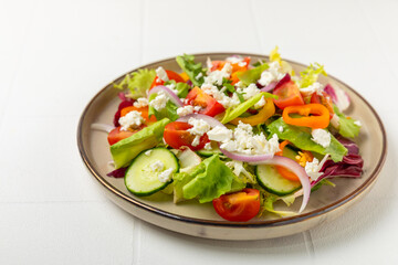 Cucumber salad on a wooden background.Homemade salad with fresh vegetables, cucumber, tomato, sweet pepper and lettuce in a plate.Vegetarian spring salad.Vegetarian diet.Healthy eating.Space for text