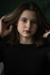 Portrait of a young beautiful long-haired girl in dark clothes in an interior studio.
