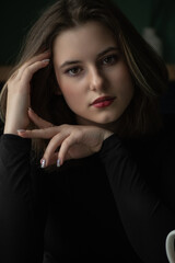 Portrait of a young beautiful long-haired girl in dark clothes in an interior studio.