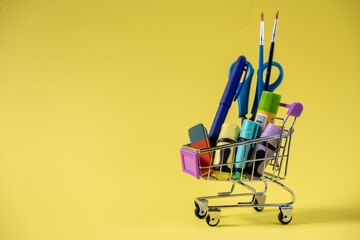 Small shopping cart brimming with vibrant educational supplies, including pens, scissors, and...