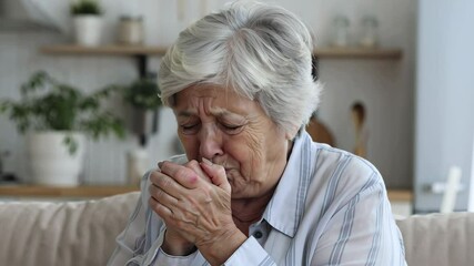 Senior woman coughing into hands, home environment. Health issues in elderly, flu, infection prevention, senior care, respiratory problems - Powered by Adobe