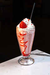 Strawberry Milkshake with Whipped Cream and Syrup in Tall Glass on Marble Table