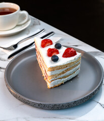 Layered Vanilla Berry Cake Slice with Cream and Fresh Fruits Served with Hot Tea in White Cup