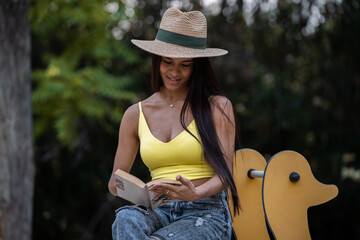 Young latin woman reading a book in a park while sitting on a seesaw