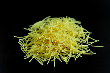 Thin vermicelli pasta lies in a pile on a black background.