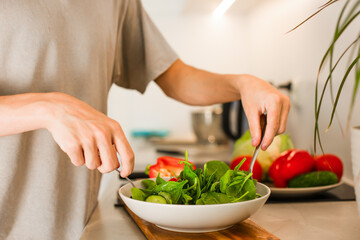 A guy is mixing while preparing a vegetarian vegetable salad with lettuce and fresh vegetables in the kitchen.