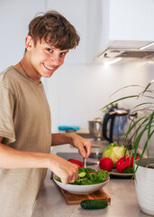 A guy is mixing while preparing a vegetarian vegetable salad with lettuce and fresh vegetables in...