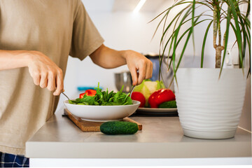  A guy is mixing while preparing a vegetarian vegetable salad with lettuce and fresh vegetables in...