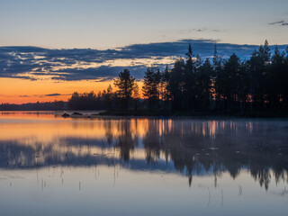 Forest and clouds are reflected in the calm water of a lake in Karelia during the white nights....