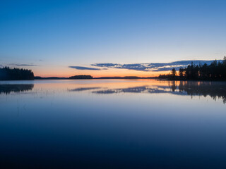 Forest and clouds are reflected in the calm water of a lake in Karelia during the white nights....