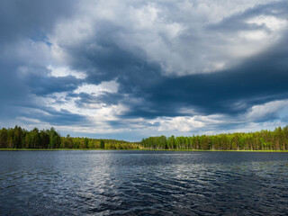 Lake, forest on the shores of the lake. Dark, rain clouds in the cloudy sky on a summer day
