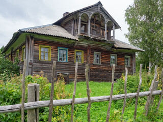 Abandoned old wooden peasant house made of logs in Karelian village, wooden fence, grassy yard