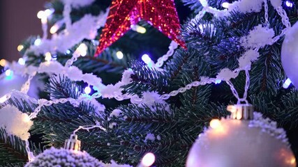 Decorative snow covers christmas tree branches decorated with white and silver ornaments and a red star, while colorful lights change colors - Powered by Adobe