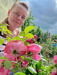 50 year old woman poses in her garden with roses in the background.