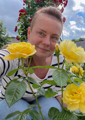50 year old woman poses in her garden with roses in the background.