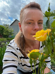 50 year old woman poses in her garden with roses in the background.