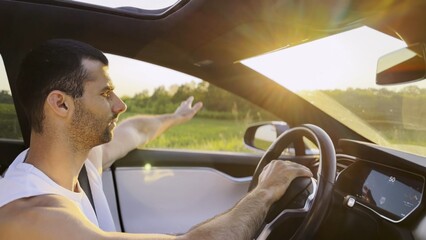 Profile of young handsome man driving a modern electric car with sunlight at background. Young male driver riding on electrical vehicle at countryside. Concept of journey and trip. Close up