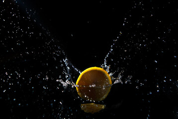 Fresh lemon slice making splash in dark water, dramatic motion freeze with flying droplets and...