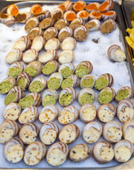 An assortment of fresh French escargots prepared with various fillings like garlic butter, cheese, and herbs, displayed on ice at a food market. Gourmet street food.