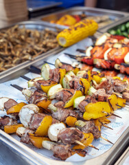 Delicious grilled meat and vegetable skewers (shashlik) displayed at a street food festival. A variety of fresh barbecue dishes on a market stall.An assortment of grilled food at a catering event