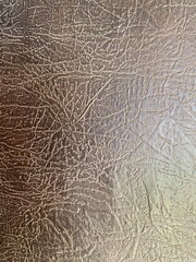High-resolution close-up texture of brown artificial leather with a cracked and metallic finish. Suitable for backgrounds, design templates, fashion mockups, or digital artwork