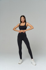 Athletic woman in black sportswear and white sneakers stands confidently with hands on hips,...