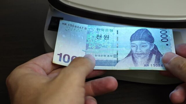 Examination of South Korean Won cash money with UV counterfeit detector. Concept of authenticity check, fight against counterfeiting of banknotes, anti fraud measures in South Korea. Close up view.