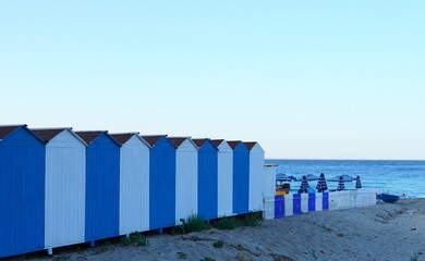 Changing rooms by the sea. The cabins are painted in alternating white and blue colors, perfectly aligned and facing the sea.