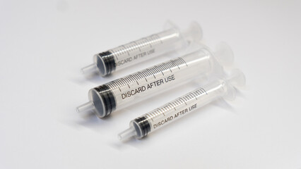 Three disposable syringes lying on a white background, with the "DISCARD AFTER USE" warning clearly visible on two of them. Medical concept of single-use sterile equipment.